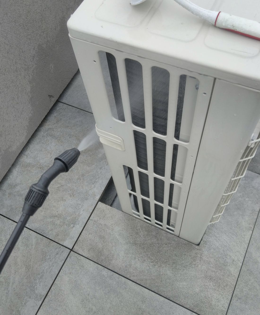 A condenser coil being cleaned with a brush and hose